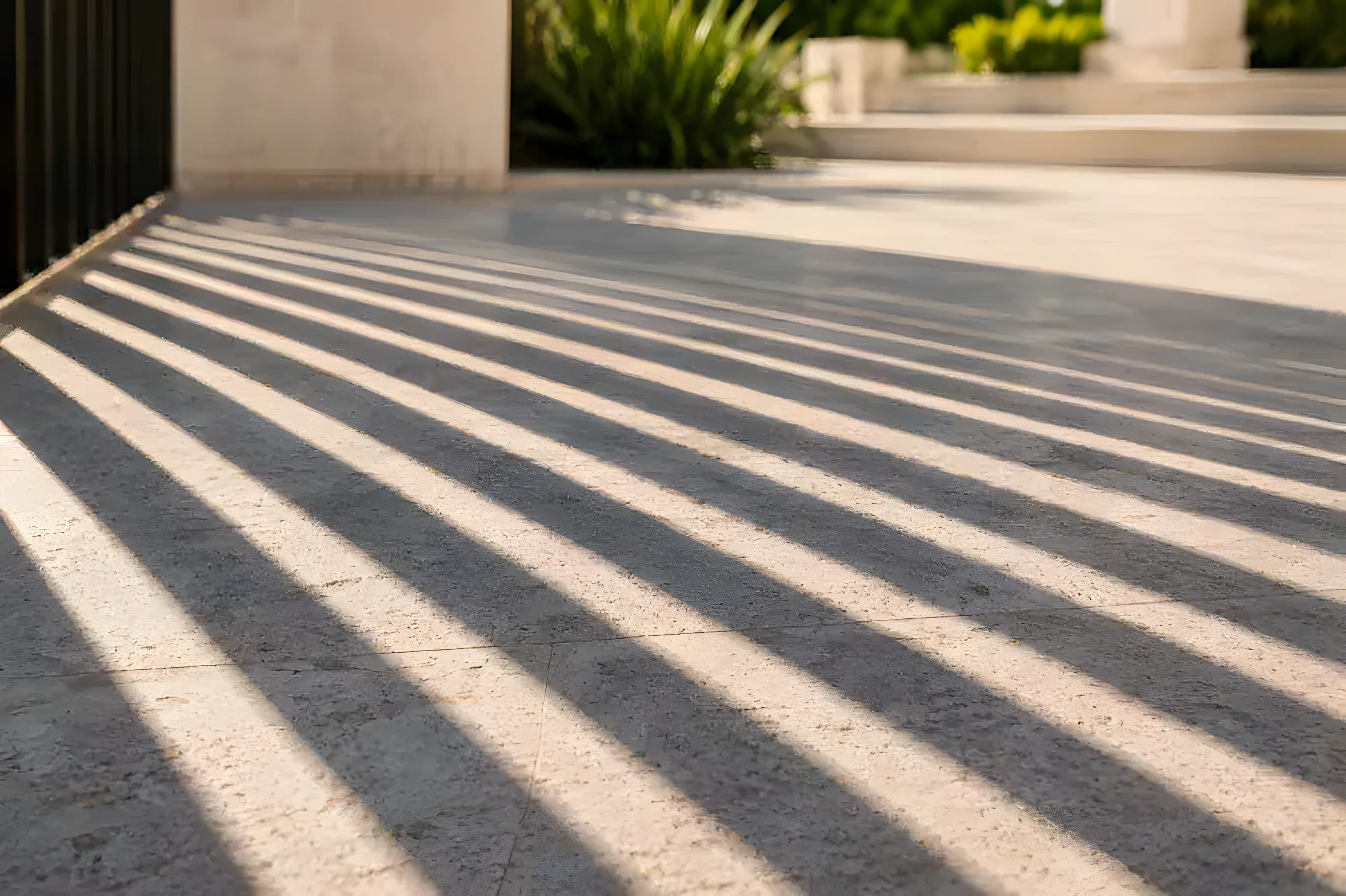 Sunlight and shadow across a paved driveway beside a gate