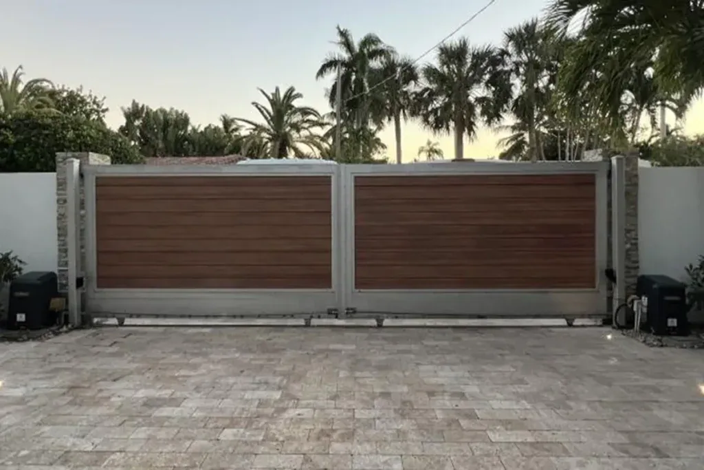 Wood-grain double driveway gate with operators on a paver driveway in Lauderhill