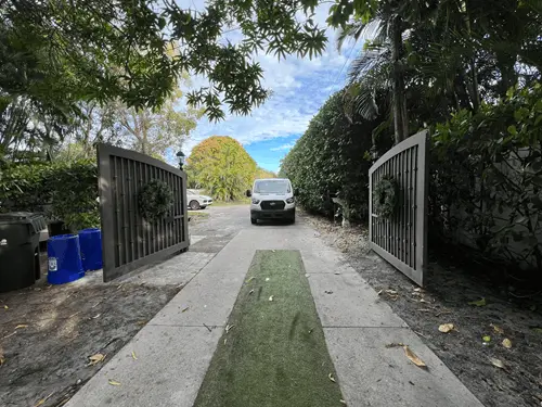 Open wooden driveway gates along a palm-lined residential drive