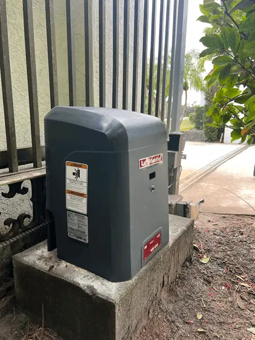LiftMaster slide gate opener on a concrete pad beside a metal fence